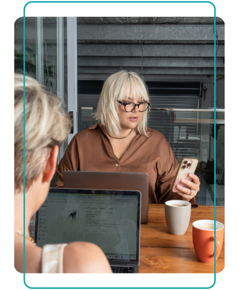 Women sitting at an office desk, with one working on laptop, the other on her mobile phone