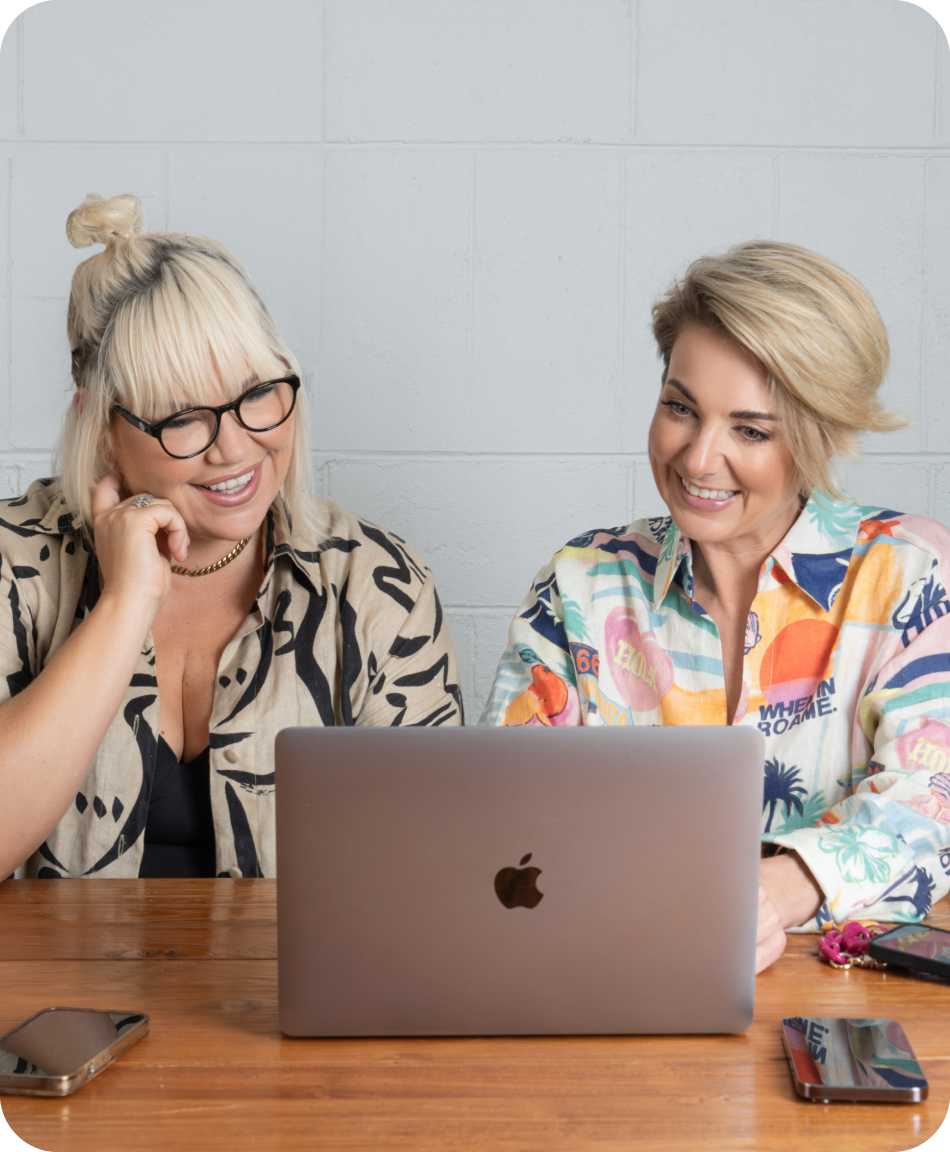 Two women smiling was they sit sharing a laptop