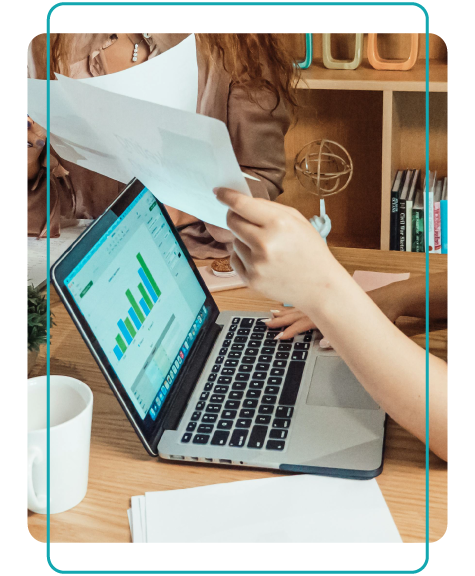 Employees hand eachother paperwork, while one woman's hands sit above a laptop with a graph showing onscreen